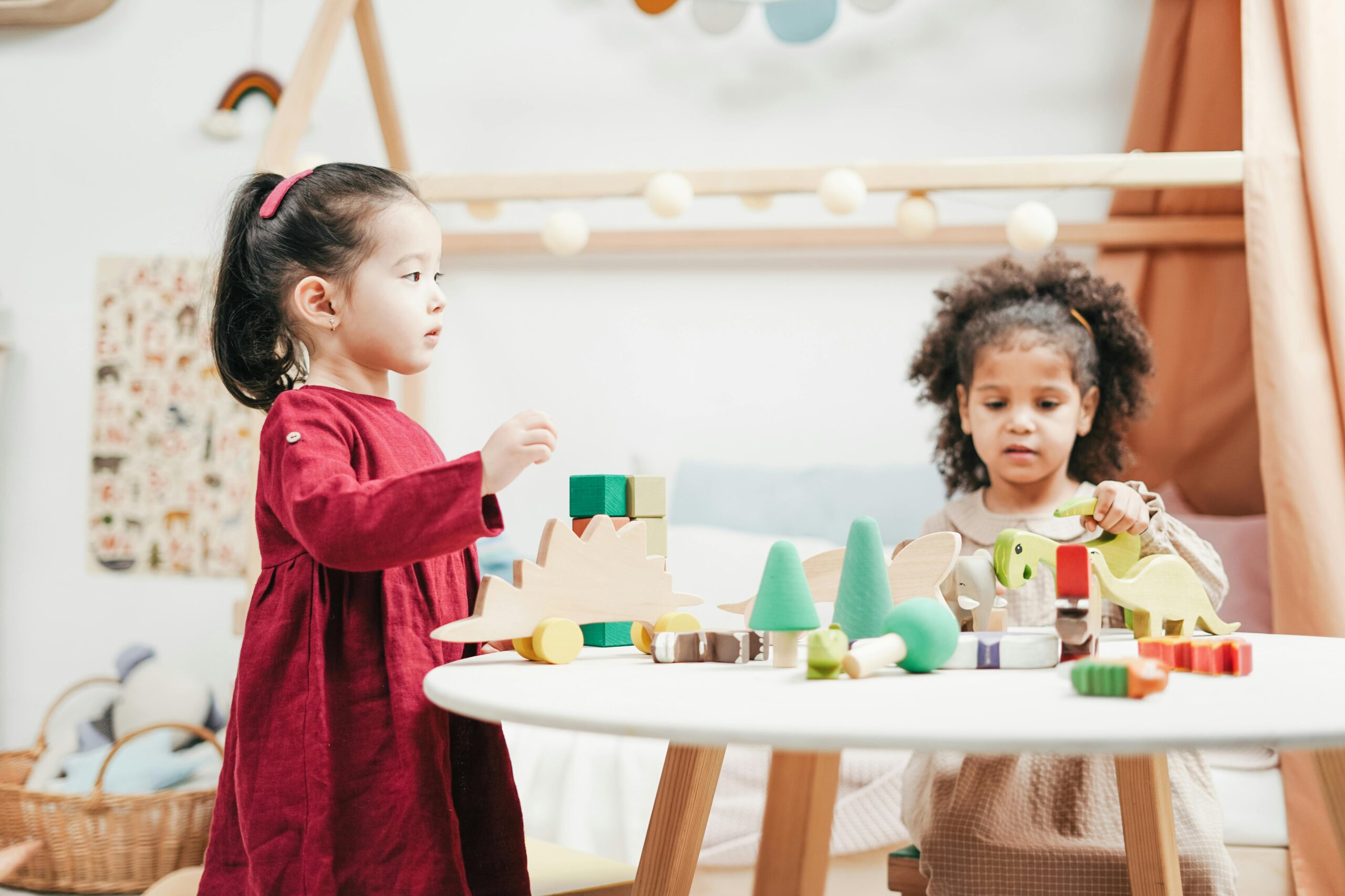 Duas meninas brincando com brinquedos numa mesa branca e com peças coloridas.