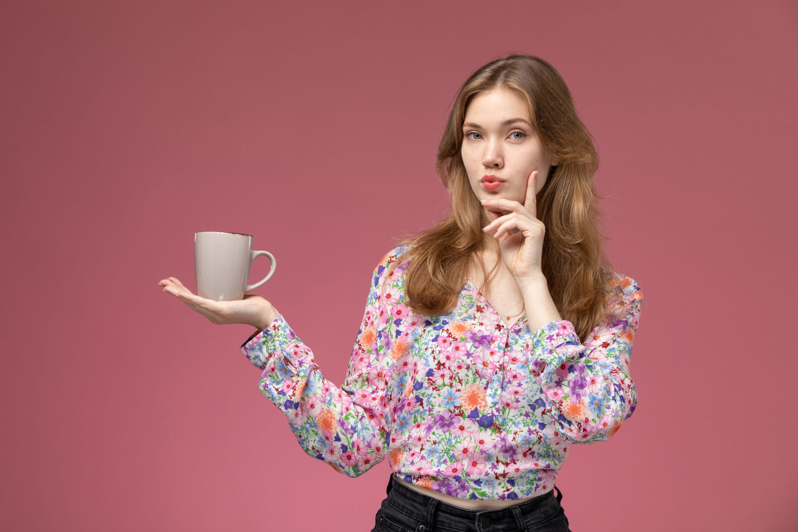 Mulher segurando uma caneca de chá para presentear alguem. Mulher loira e fundo cor rosa escuro.